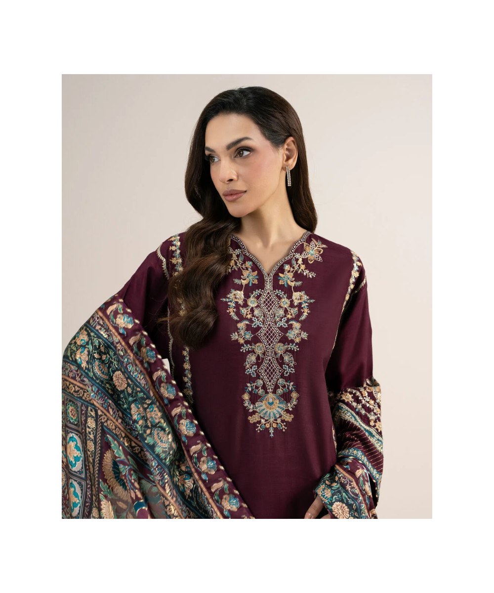 A woman modeling a deep maroon traditional embroidered kurta with a matching patterned dupatta against a plain beige background.